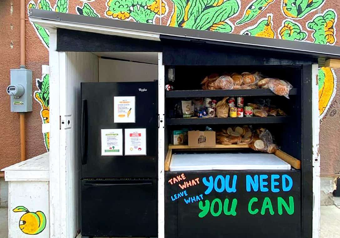 Roofed structure with a community fridge and shelves holding bread and other food.