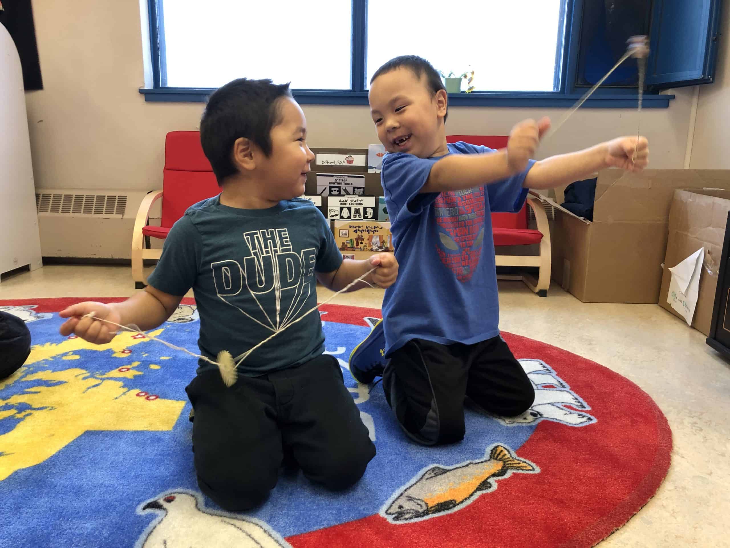 Two children are playing with string toys and smiling.
