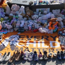 Memorial with flag placed on the ground that reads "Every Child Matters" with children's shoes and stuffed animals surrounding it.