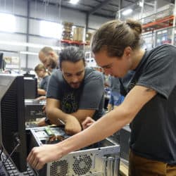 Two workers looking at the inside of a computer and talking to each other.