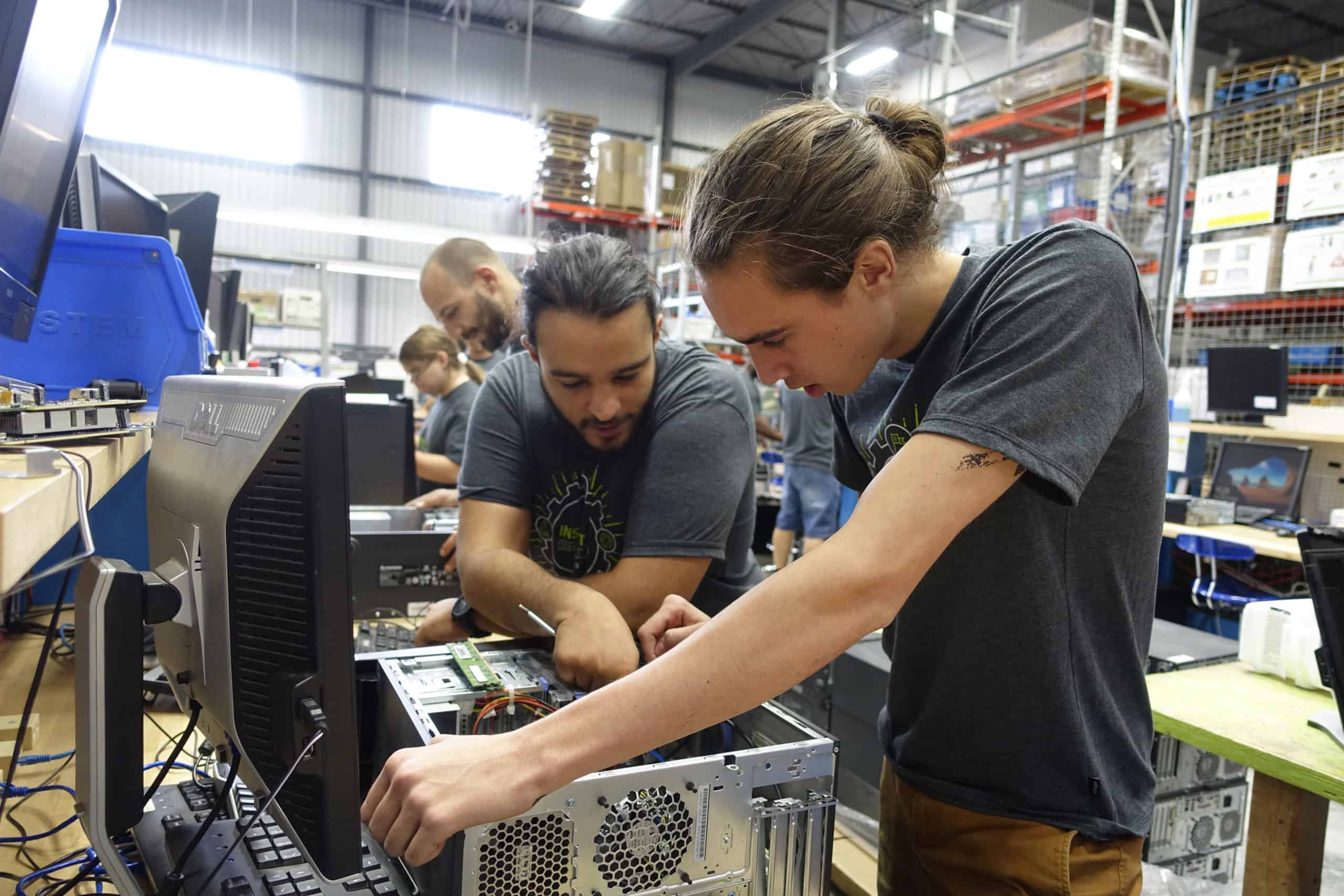 Two workers looking at the inside of a computer and talking to each other.