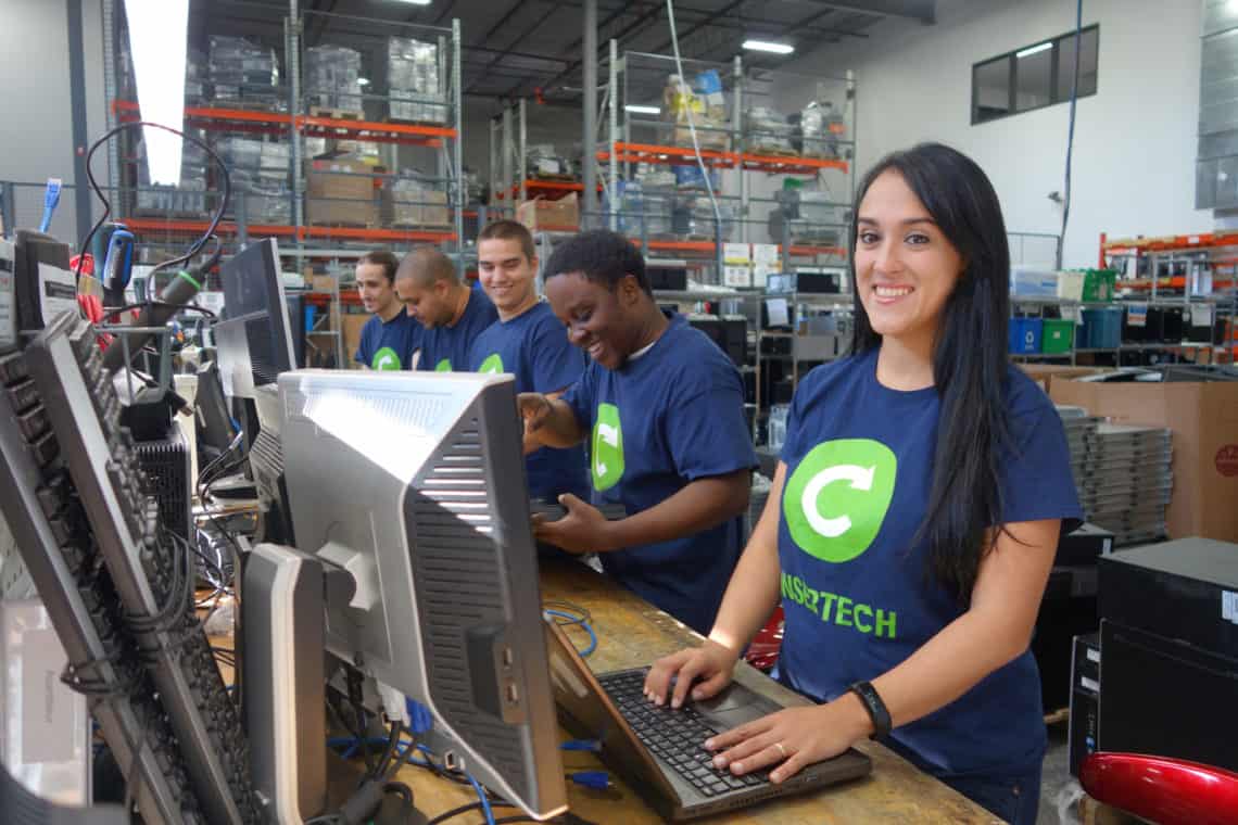 Five workers wearing Insertech t-shirts smiling, each in front of a piece of a computer inside a warehouse.