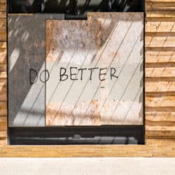 The words Do Better are spray painted on a boarded up window