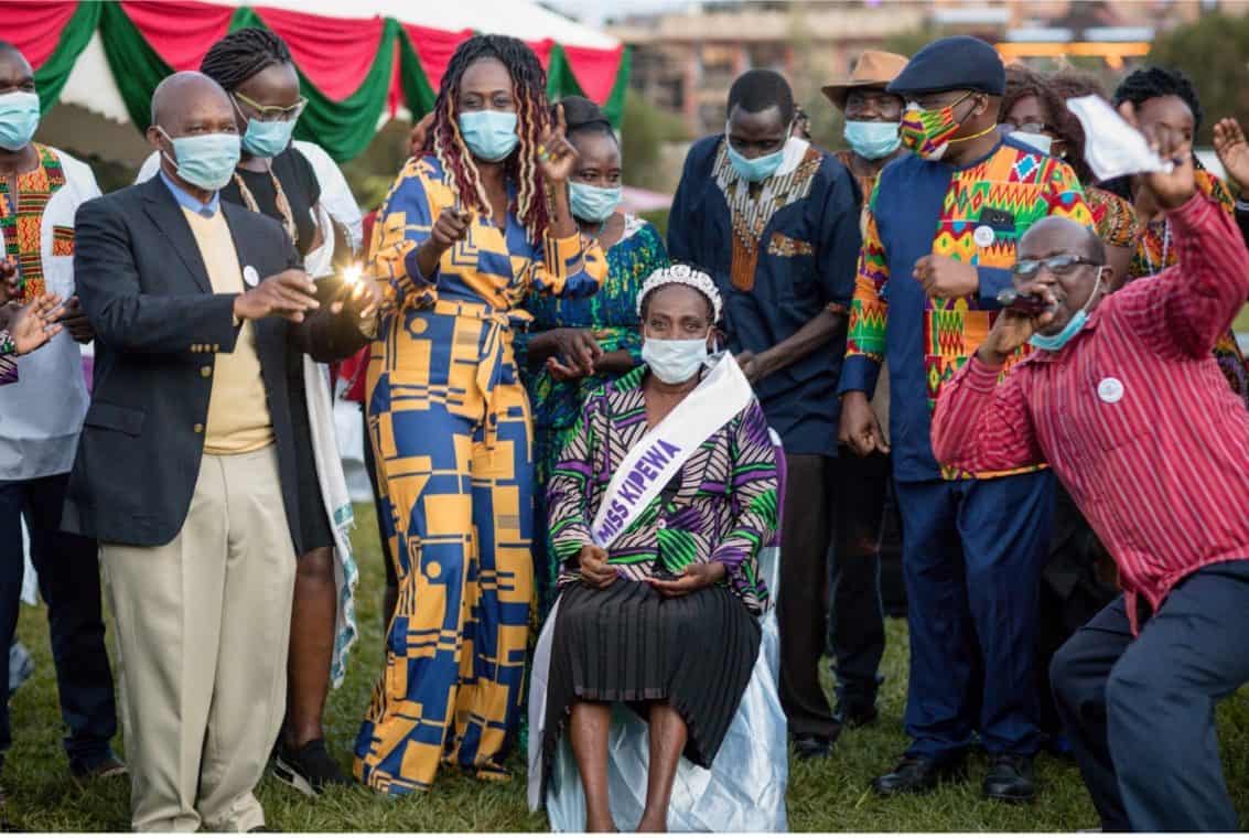 A group of people celebrating with masks on. One person is seated with a sash that reads, "Miss Kipewa."