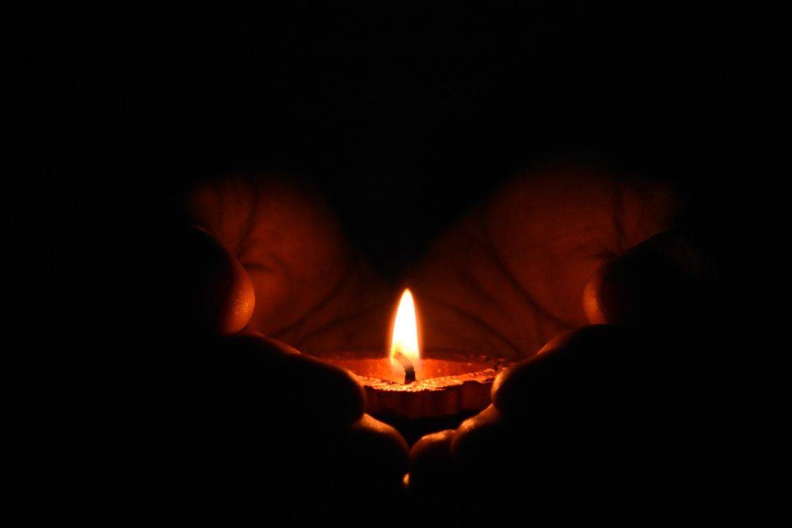 Hands holding a lit candle in the dark