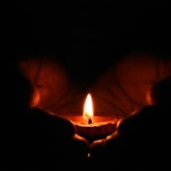 Hands holding a lit candle in the dark