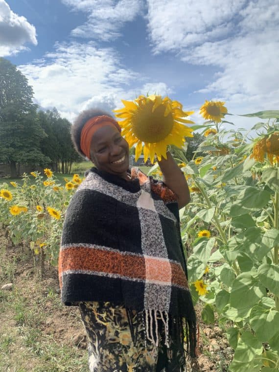 Jacqueline Dwyer, Founding Member of the Toronto Black Farmers and Growers Collective poses with sunflowers growing in a field.