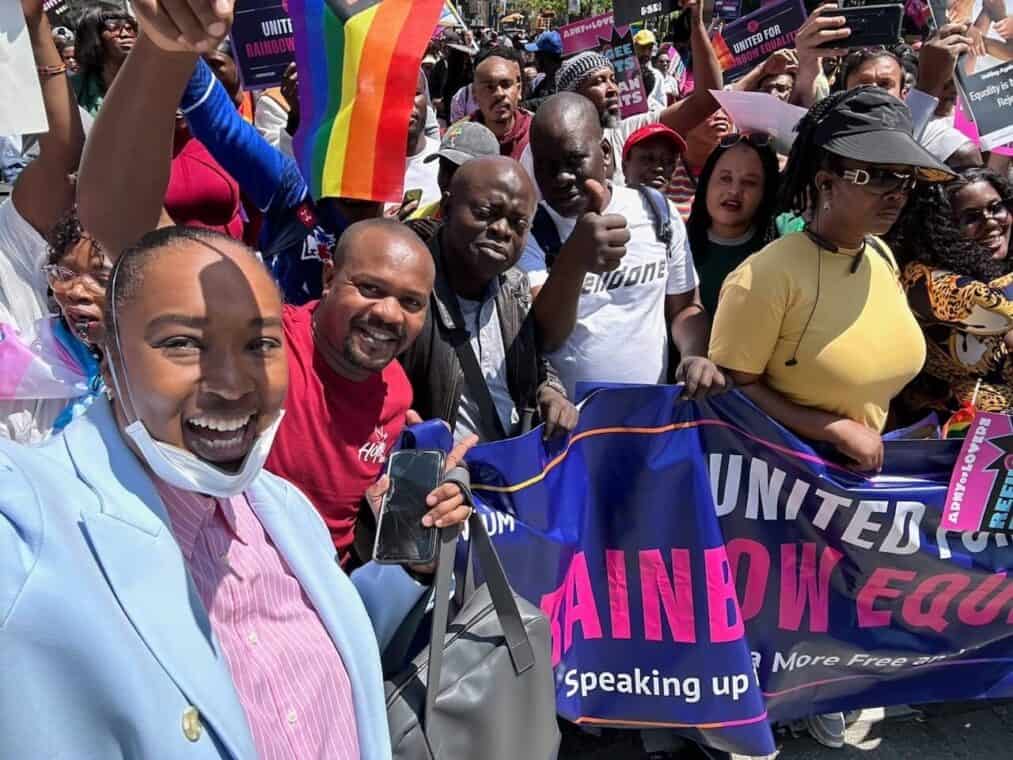 Cheerful people holding a "United for Rainbow Equality" banner outside with a pride flag.