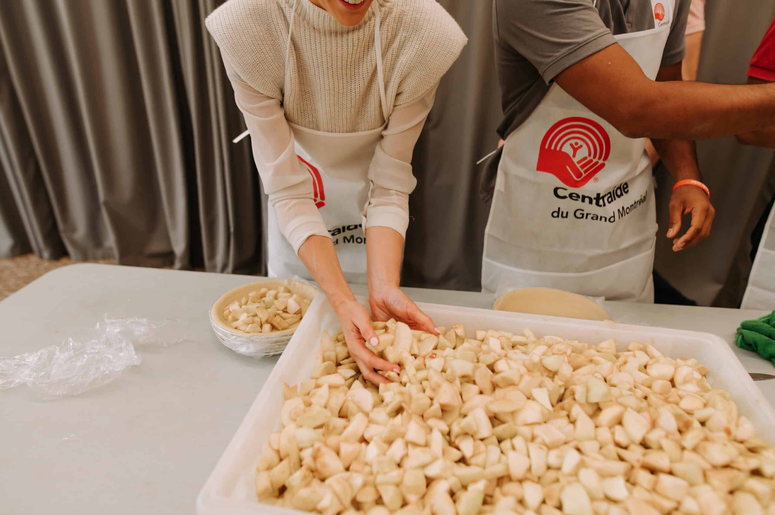 People with Centraide du Grand Montréal aprons in front of a large container of cut apples.