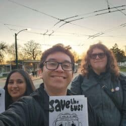 Three people smiling and holding pamphlets that say "save the bus!"