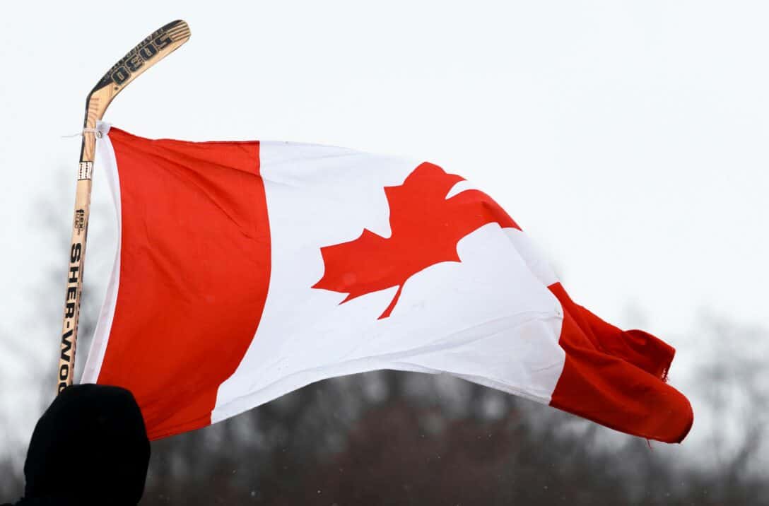 Canada flag being held up in the air by a hockey stick.