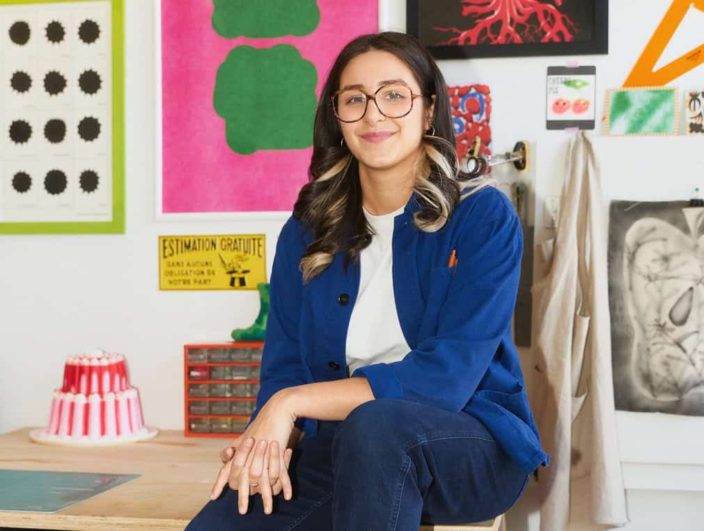 Maïa Faddoul smiles at the camera with artwork hanging behind her.