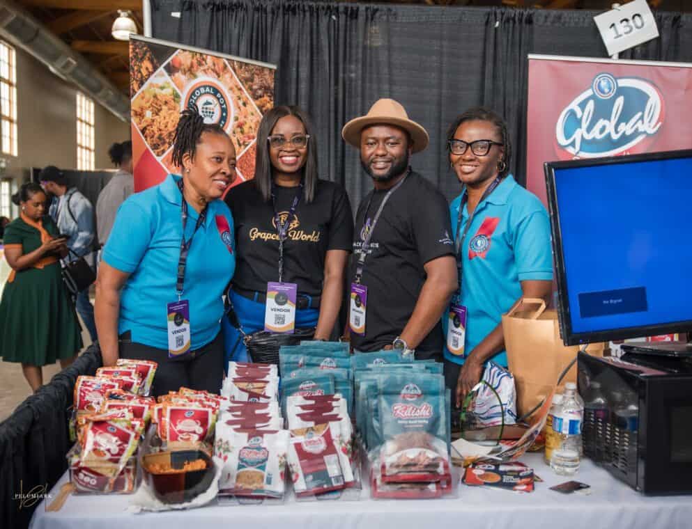 Four people pose for the camera at a booth with packaged foods on the table and banners behind them.