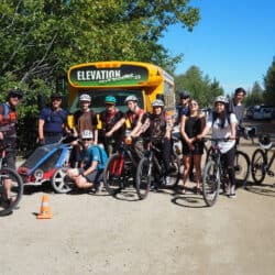 The Elevation Outdoors team on bicycles in front of a school bus.