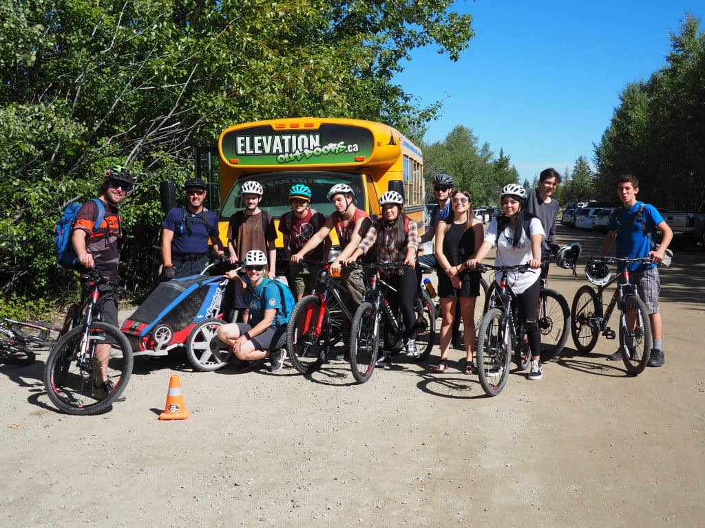 The Elevation Outdoors team on bicycles in front of a school bus.