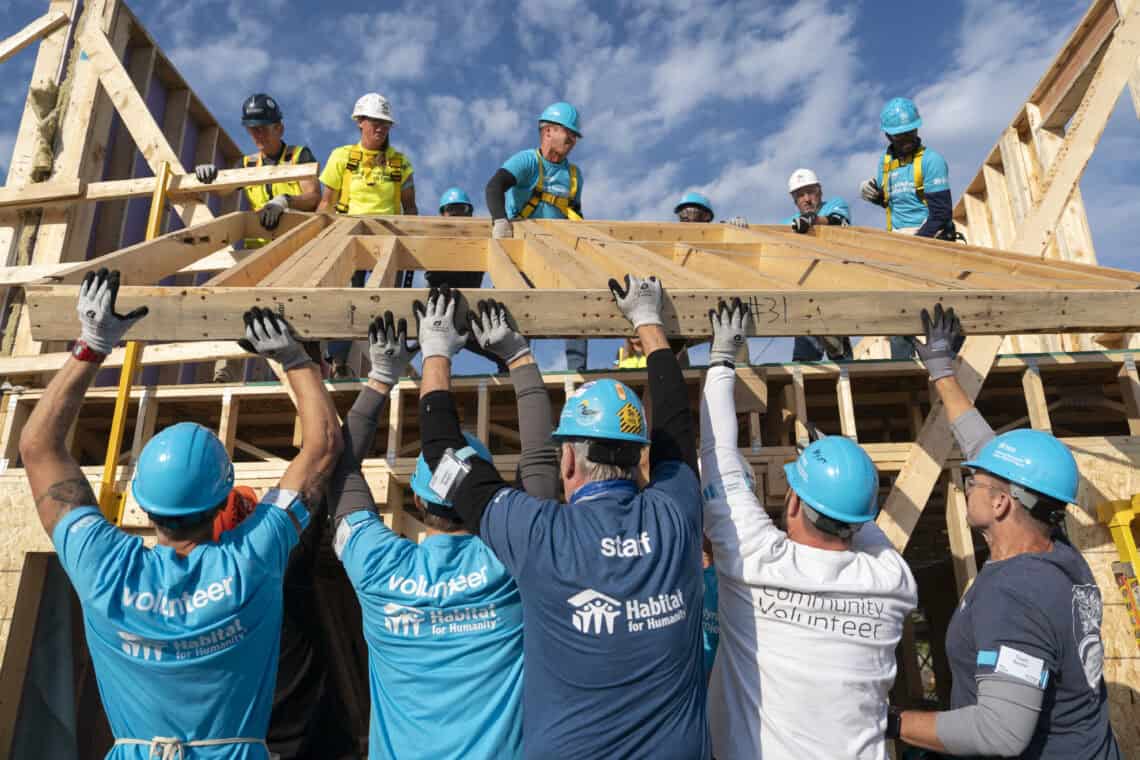 Habitat for Humanity volunteers lift a wooden frame at a build site.