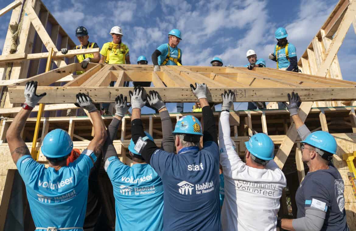 Habitat for Humanity volunteers lift a wooden frame at a build site.