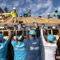 Habitat for Humanity volunteers lift a wooden frame at a build site.