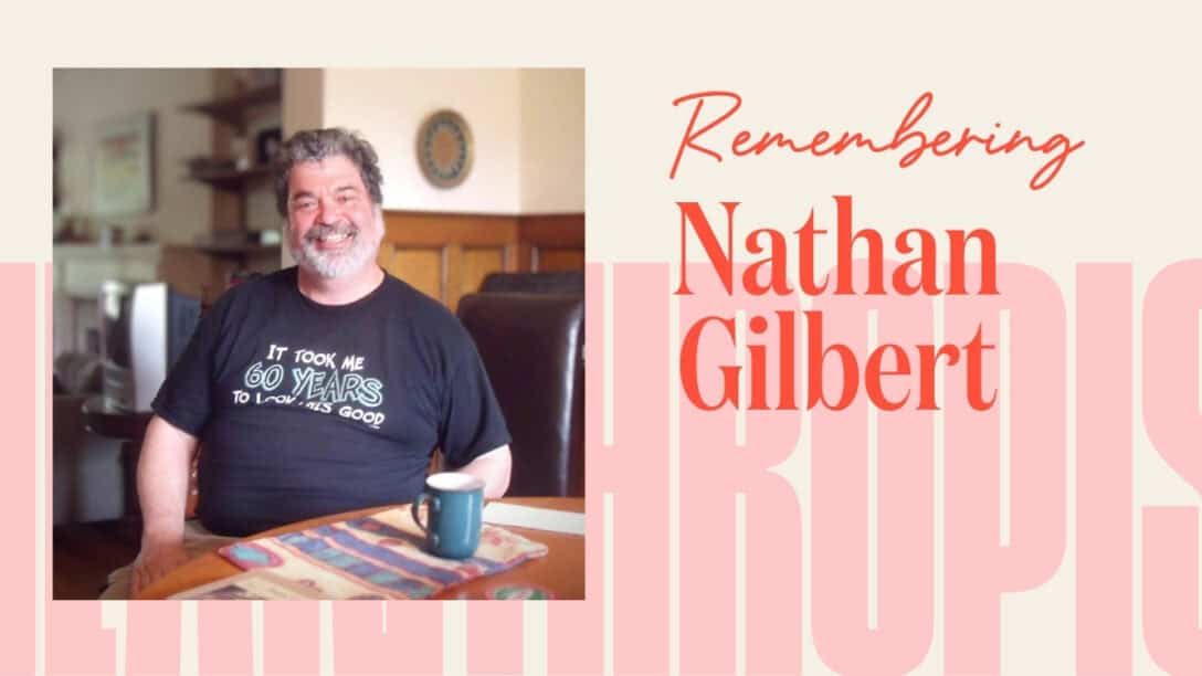 Photo of Nathan Gilbert sitting at a table smiling. There is a frame around the picture that says, "Remembering Nathan Gilbert"