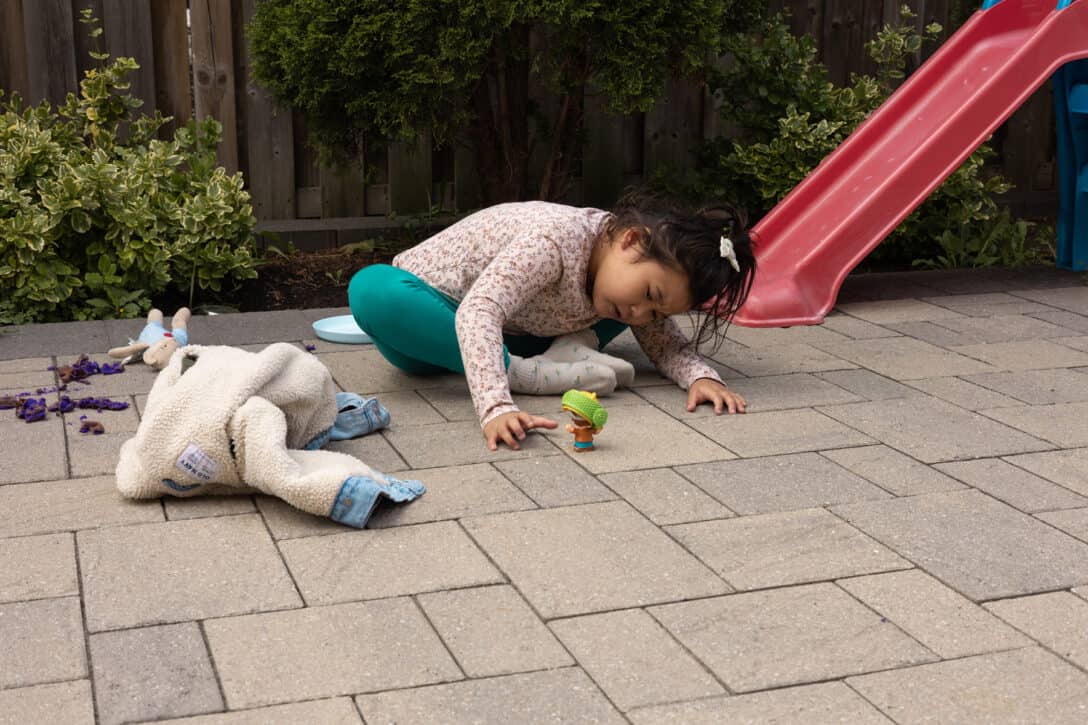 A child sitting on pavement leaning down to look at a toy.