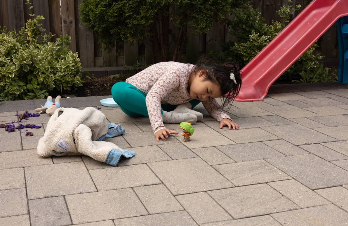 A child sitting on pavement leaning down to look at a toy.