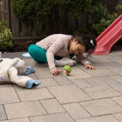 A child sitting on pavement leaning down to look at a toy.