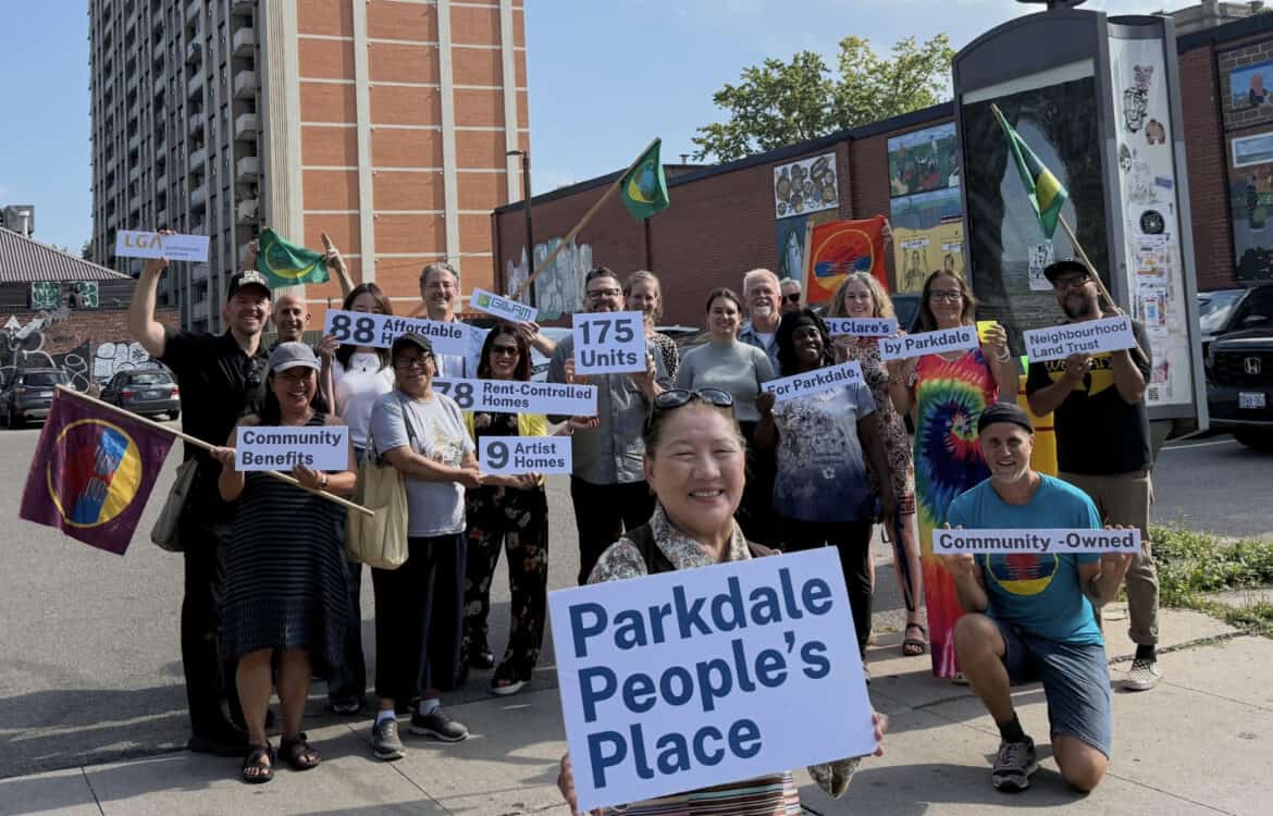 A photo of smiling members of the Parkdale Neighbourhood Land Trust in front of Parkdale People's Place.