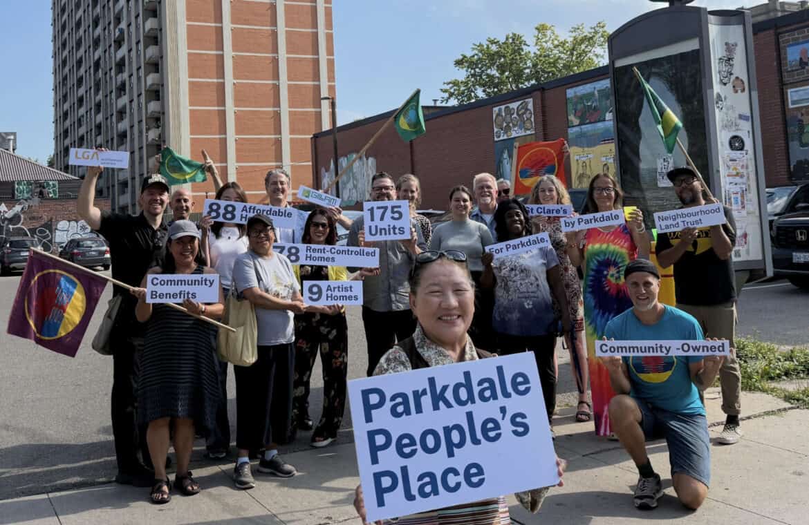 A photo of smiling members of the Parkdale Neighbourhood Land Trust in front of Parkdale People's Place.