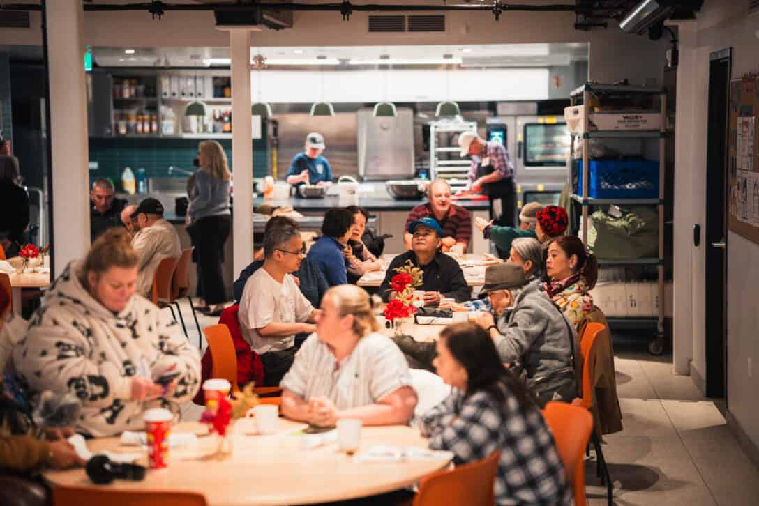 A photo of people having lunch, with volunteers in the background, at Sumac Community Food Centre in downtown Toronto.