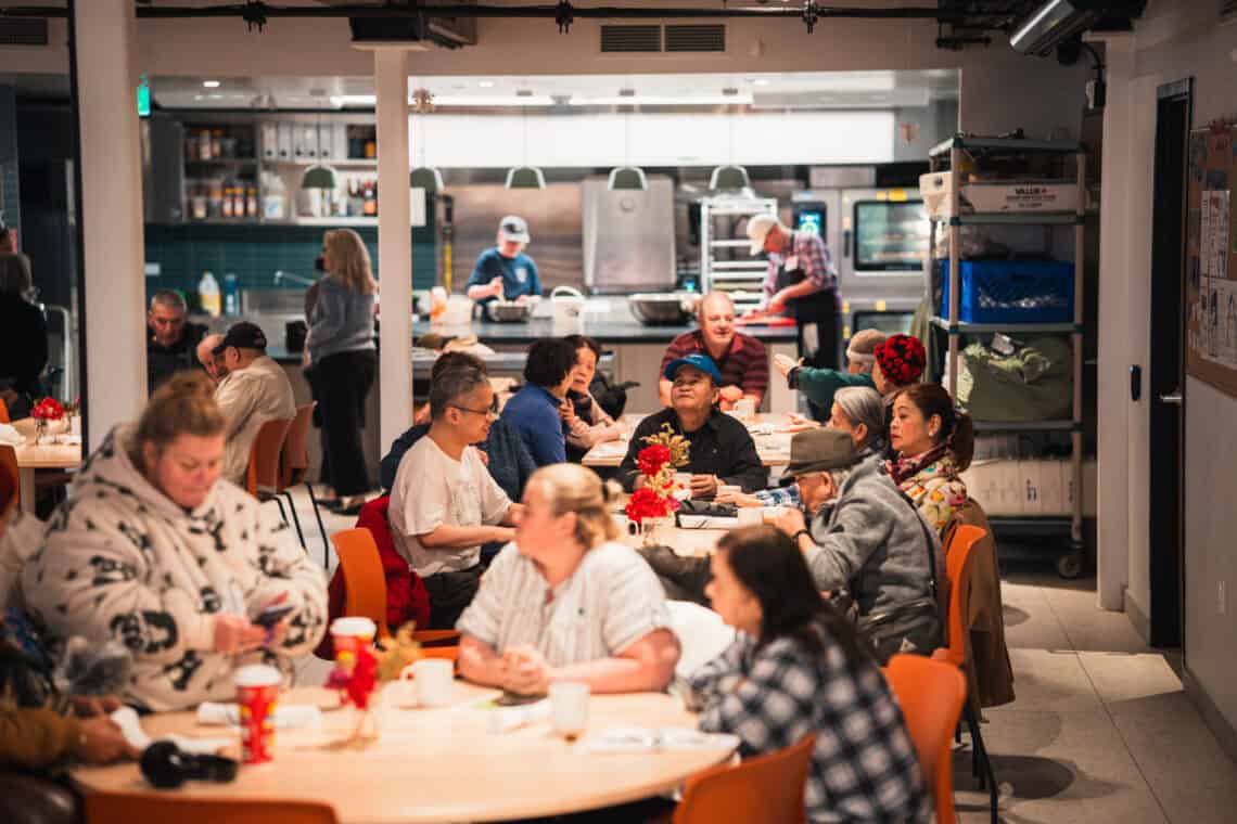A photo of people having lunch, with volunteers in the background, at Sumac Community Food Centre in downtown Toronto.