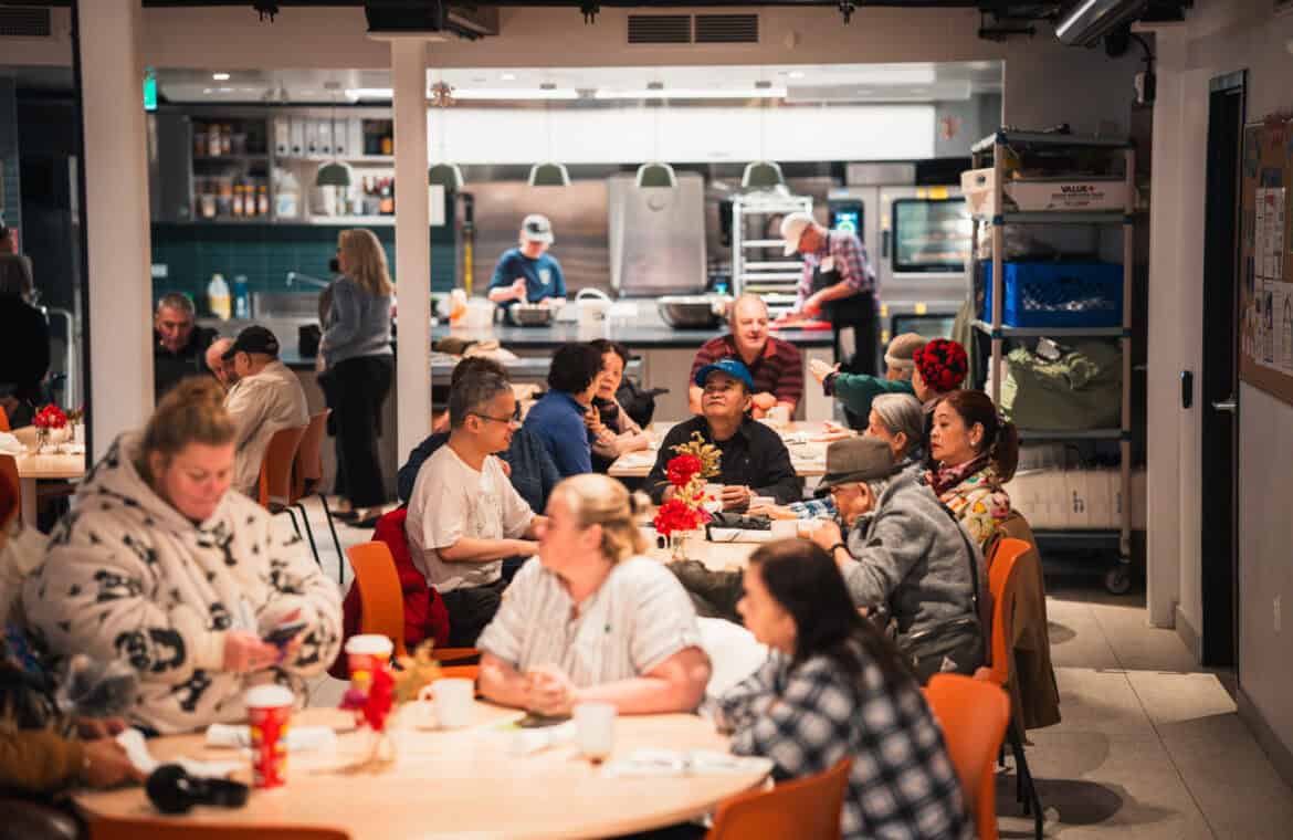 A photo of people having lunch, with volunteers in the background, at Sumac Community Food Centre in downtown Toronto.