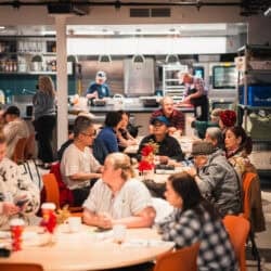 A photo of people having lunch, with volunteers in the background, at Sumac Community Food Centre in downtown Toronto.
