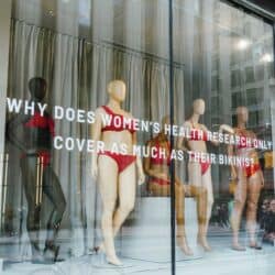 A photo shows bikini-clad mannequins displayed behind glass with the words "Why does women's health research only cover as much as their bikinis?"