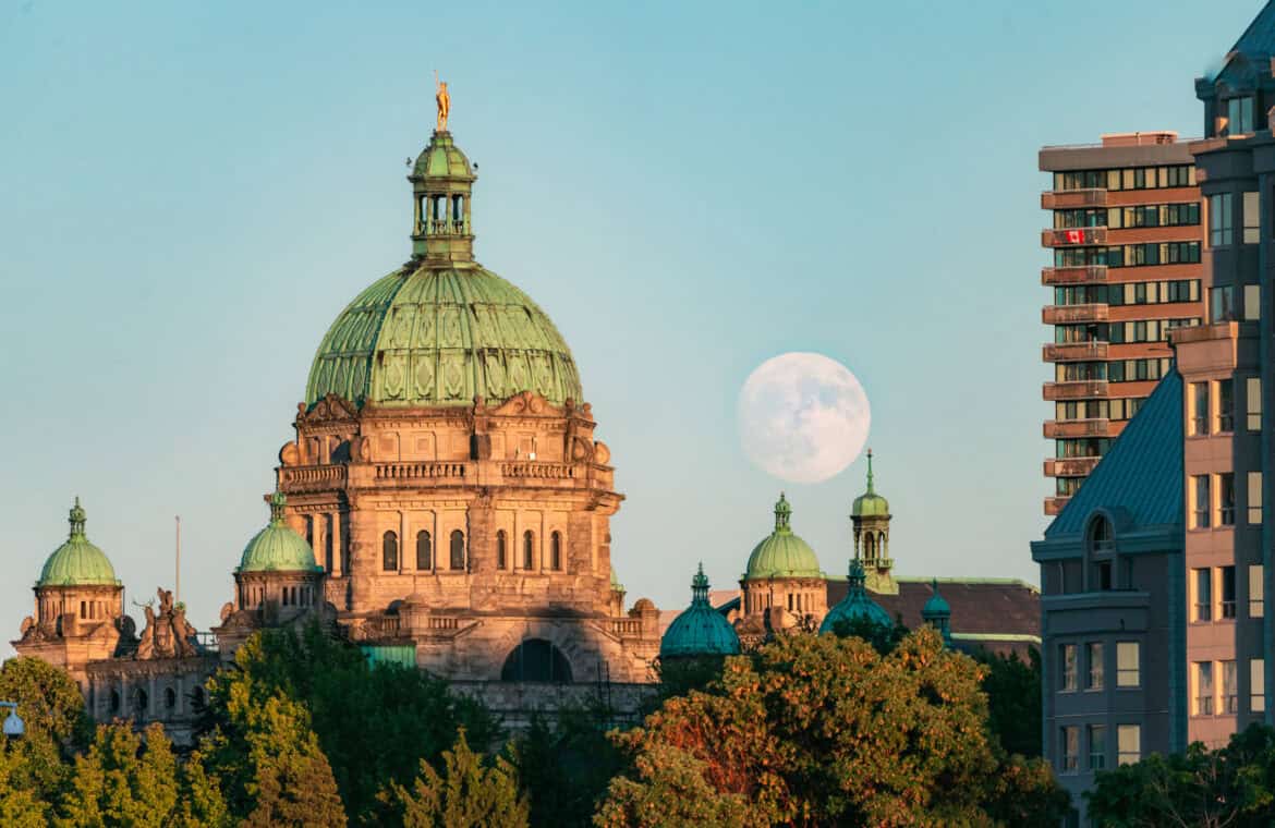A photo of the moon rising over the Parliament Buildings in Victoria, BC, during sunset.