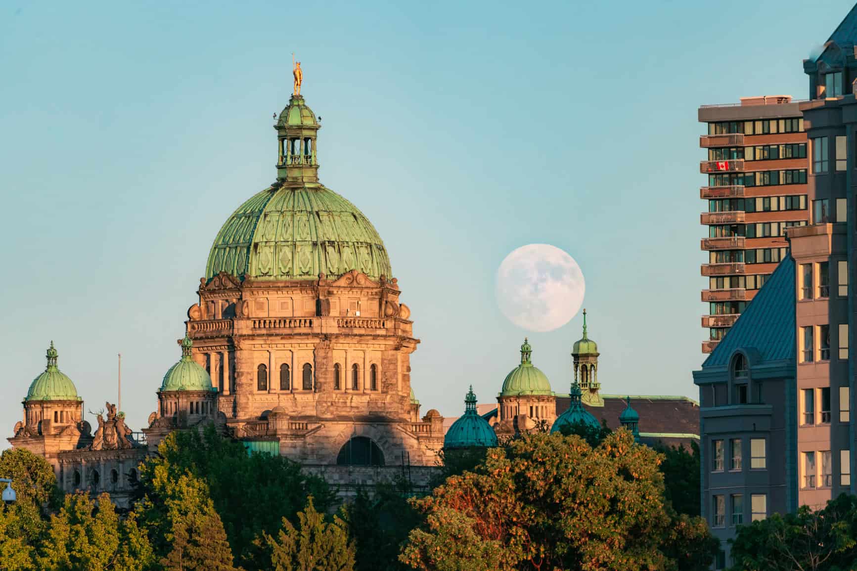A photo of the moon rising over the Parliament Buildings in Victoria, BC, during sunset.